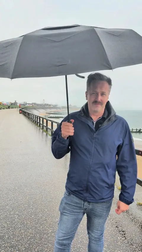Weather man Chris Blanchett holds a black umbrella 