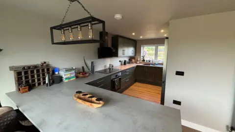 Luke Deal/BBC A newly renovated kitchen. It has been decorated in a grey colour and there is a large kitchen island. 