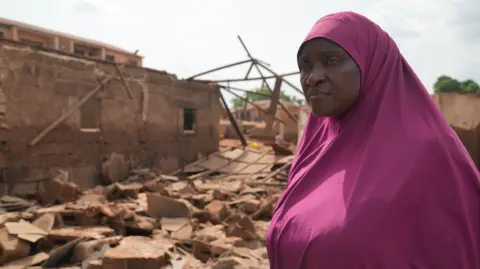 Gift Ufuoma Ramat Sulaiman standing outside a destroyed building