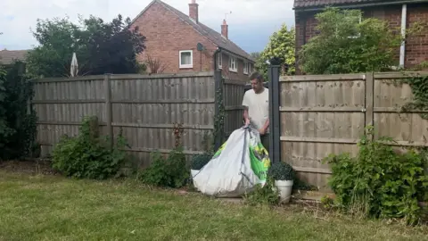 Adam Castledine taking a bag of garden waste out of his garden and on to a grass verge