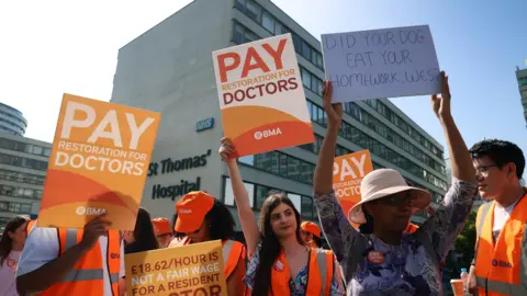 EPA Doctors on strike, holding up placards calling for more pay, one reads: "did your dog eat your homework, Wes?" in reference to Health Secretary Wes Streeting