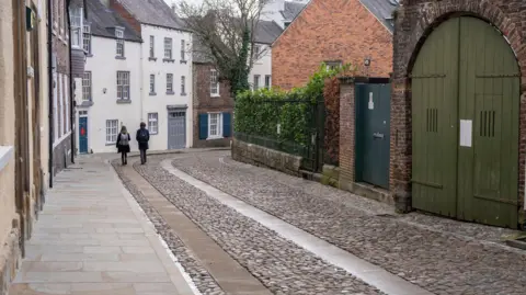 Durham City Council Cobbled street and two people walking along it in the background. 