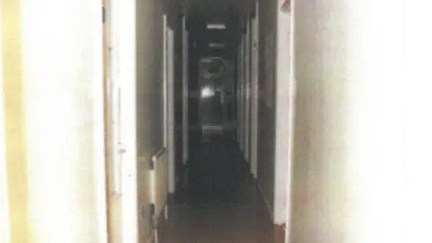 West Yorkshire Police A corridor in a children's home with multiple doorways off each side. The walls are painted white and there is dark wooden flooring. It looks gloomy with little light the further it goes on