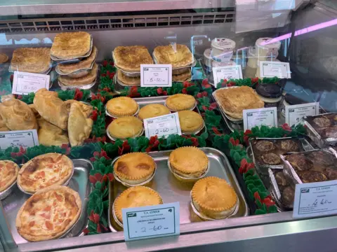 A glass cabinet containing food that includes meat pies, pasties and faggots.