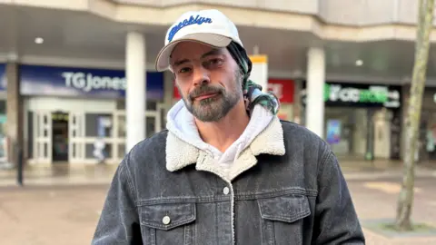 BBC Man wearing cap and a black denim jacket looking at camera