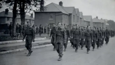 Heritage Service, Dumfries and Galloway Council A black and white picture of men marching past houses 