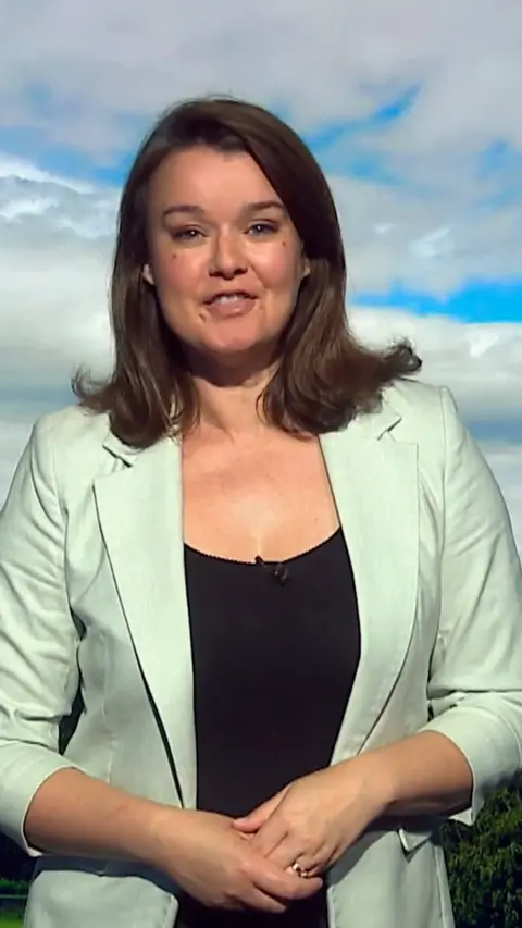 Gillian Smart - Woman with shoulder length dark hair, wearing a mint blazer and standing in front of a weather green screen