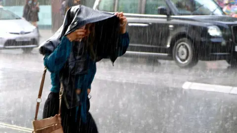 A woman holds her jacket over her head as rain pours down in London