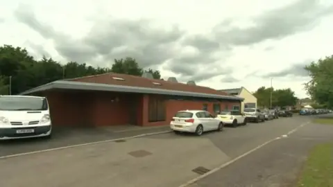 Exterior of a brick building with several cars parked on the road in a line next to the entrance of the children's home