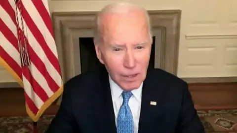 Joe Biden speaking connected  a virtual telephone  with American emblem  down  him