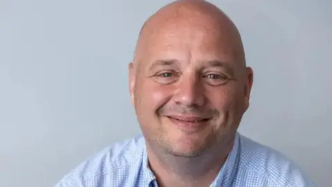 A man with bald head and a pale blue checked shirt