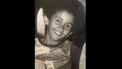 A black and white photo of Desmond, at eight years old. He is smiling and wearing a Superman T-shirt