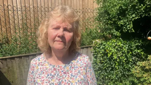 Photograph of Sarah Walker form the local residents association. She is pictured in front of a wooden fence which has been erected at the back of her garden.