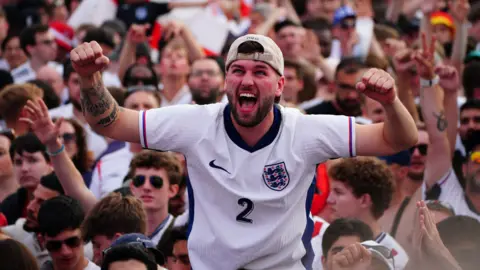 PA Man in England shirt sits on someone's shoulders in a crowd cheering