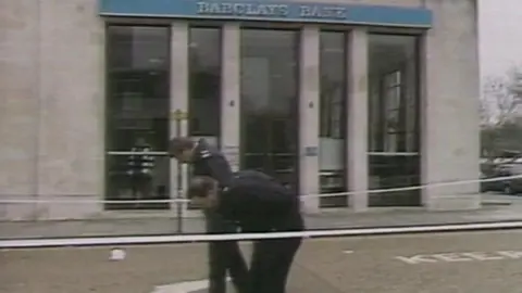 A photo of Barclays Bank from 1988 with police tape in front of the white brick building. Two officers are stood outside.