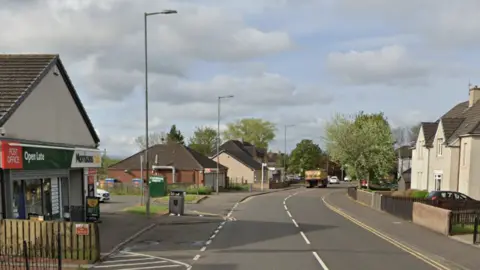Google A Post Office and Morrisons shop on the left side of a road with houses opposite