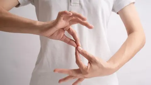 Person in white top holding their hands in a position to illustrate sign language.