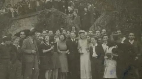 Gwrych Castle Trust Archive Black and white picture of people standing by the garden steps of the castle. Among the people is a bride and groom, wearing a wedding dress and suit