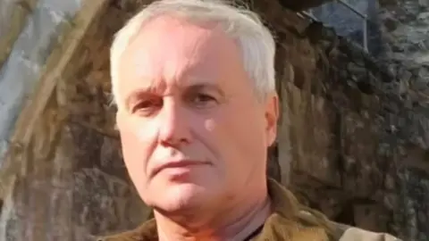 Rob Taylor Rob Taylor has short white hair and is clean shaven. He looks down to the camera with a blank expression on his face. 