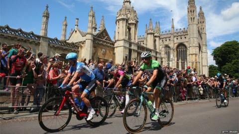 Four Tour de France cyclists slowly pedalling down King's Parade, Cambridge, in front of crowds in 2014