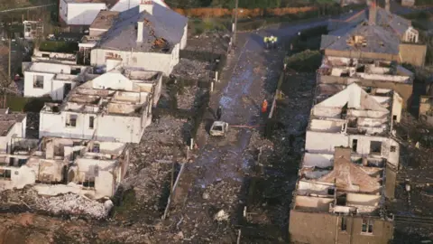 As imagens Getty são uma fileira de casas destruídas em Locorbi. Seus telhados foram soprados, seu interior foi destruído e os detritos foram jogados através da terra. Um carro queimado é visto no meio da estrada e apenas alguns policiais e trabalhadores de emergência são visíveis na estrada.