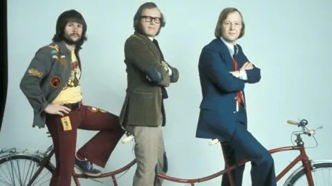 The Goodies on their 'trandem' bicycle. Bill Oddie is at the rear, Graeme Garden is in the centre and Tim Brooke-Taylor is at the handlebars
