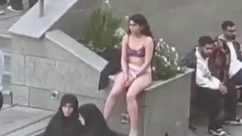 Telegram Screengrab of a video showing an Iranian woman sitting in her underwear at the Science and Research Branch of Islamic Azad University in Tehran, Iran. There are groups of other people