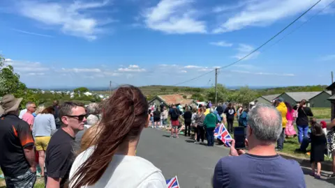 A crowd of people waiting for teams to cross the finish line. Some people are holding Union Jack flags.