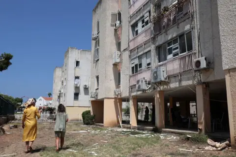 Getty Images Residents walk next to a building in the Israeli coastal town of Acre 
 damaged by a rocket fired from Lebanon by Hezbollah on 25 August 2024