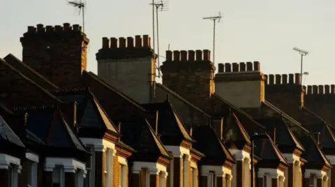 A generic image of half a dozen chimneys and part of upper floors of homes, seen from the outside. 