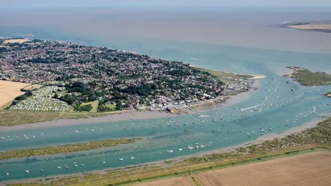 John Fielding/Wikimedia Commons An aerial view of West Mersea in Essex, showing residential areas surrounded by water with several boats.