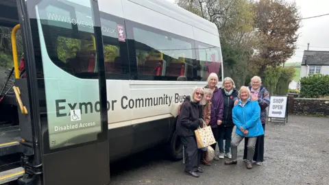 Exmoor Community Bus Association Six ladies posing in front of the minibus that they travel on. They have coats and bags and are smiling. 