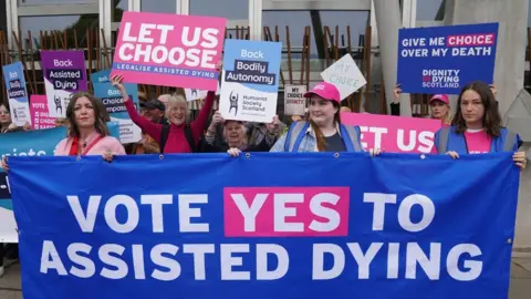 Protesters outside the Scottish Parliament hold up colourful signs in favour of assisted dying 