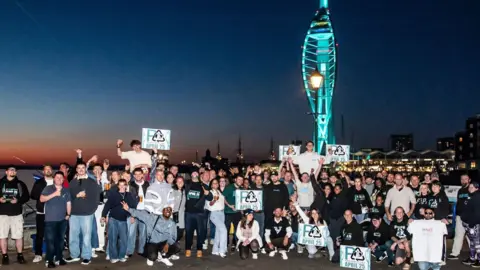 Feather and Lens Media A crowd of people at night in front of the Spinnaker Tower, which is lit up in green light