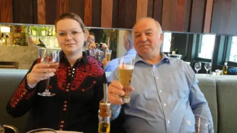 Sergei and Yulia Skripal holding up glasses of alcohol, Yulia is holding a wine class and Sergei a beer.