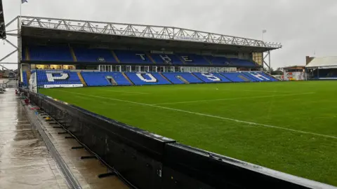 Emma Baugh/BBC An empty, two-tier stand at Peterborough United's ground. Most of the seats are blue, but there are white sets spelling out the the words "The Posh". ABout half of the green pitch can be seen in front of the stand.