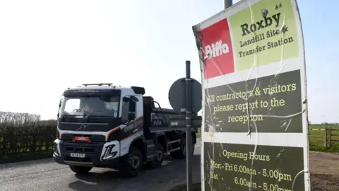 A small tipper lorry passing a roadside sign which reads: Biffa Roxby landfill site and transfer station.
