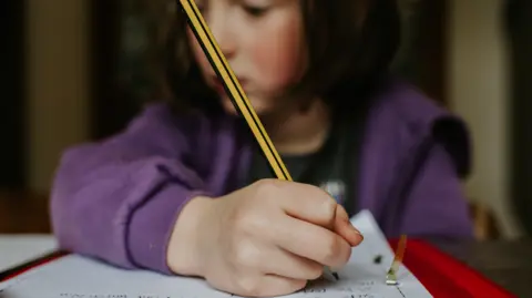 Getty Images A young girl studying. Her face is blurred but she is holding a pencil over a piece of paper.