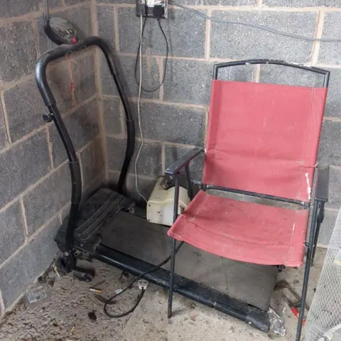 RSPCA A black treadmill situated in a corner against a grey brick wall with a red fold up chair next to it.