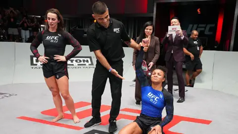 Getty Images Ffion Davies on the left looks at the floor with her hands on her hips. On the right, Cassia Moura has her hand raised by the referee with an expression of relief on her face after her victory in the women's bantamweight championship match