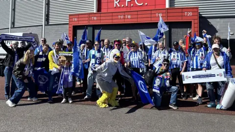 A group of Brighton and Hove Albion fans standing outside a red stadium.