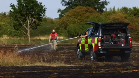 Reuters Firefighters work at the scene of a wildfire in Northolt, north-west of London on 12 August 2025.