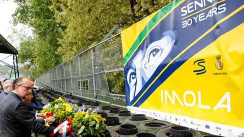 People lay flowers under a banner paying tribute to Ayrton Senna at Imola 