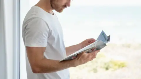 A man in a white t-shirt reads a magazine