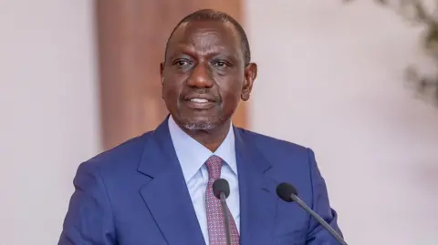 A close-up of William Ruto wearing a blue suit and a dotted tie 