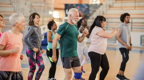 Getty Images A stock image showing a group of men and women in brightly coloured clothes smiling and dancing in a Zumba class.