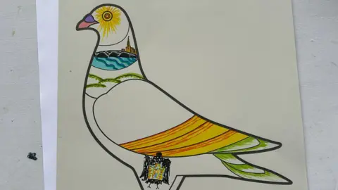 Permission 2 A paper template of a pigeon with drawings of a church and yellow and green banding.