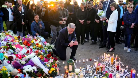 Liberal Leader Mark Carney kneels at floral tributes as he takes a moment after lighting a candle at a memorial for the Lapu Lapu Day block party tragedy in Vancouver, B.C., on Sunday, April 27, 2025.