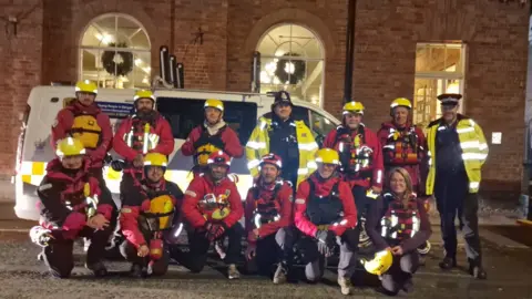 WMSAR The team and two police officers pose for a photo in uniform by a large white van.