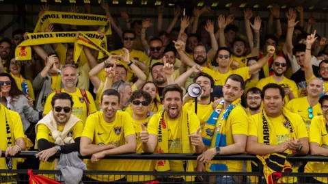 Dozens of Spanish football fans wearing Harborough Town football shirts